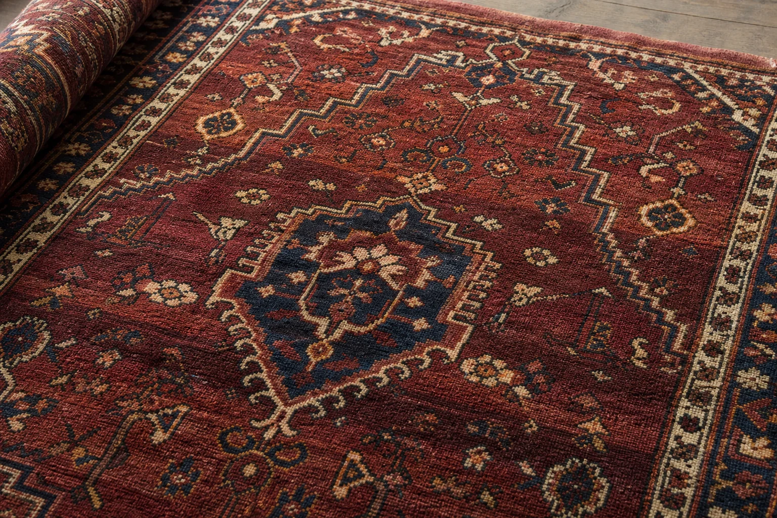 Close view of a hand-knotted Persian rug with subtle horizontal variation in the red field known as abrash
